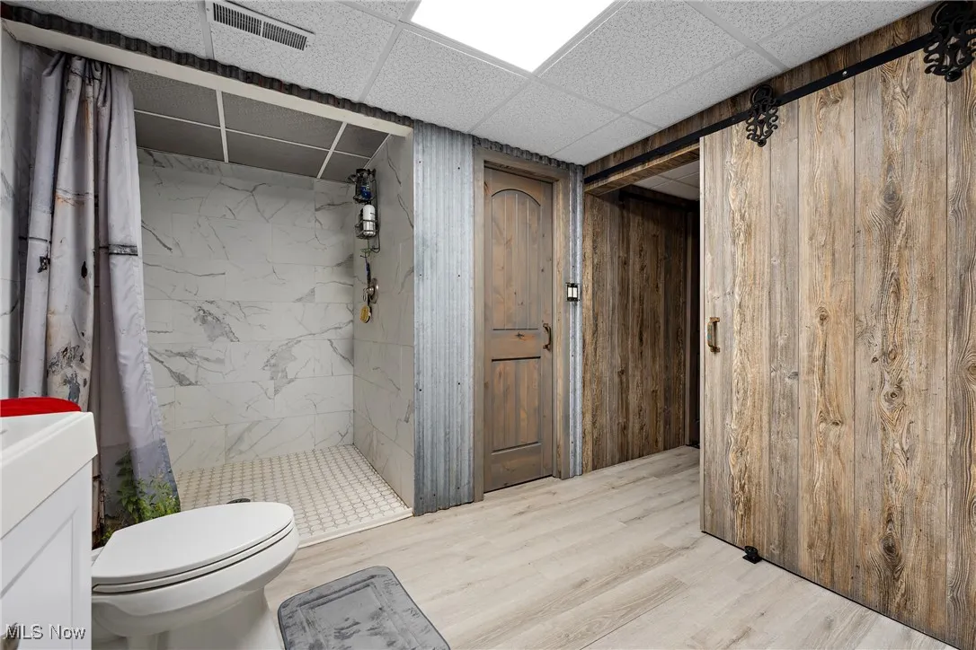 Bathroom featuring wood walls, a stall shower, toilet, and wood finished floors