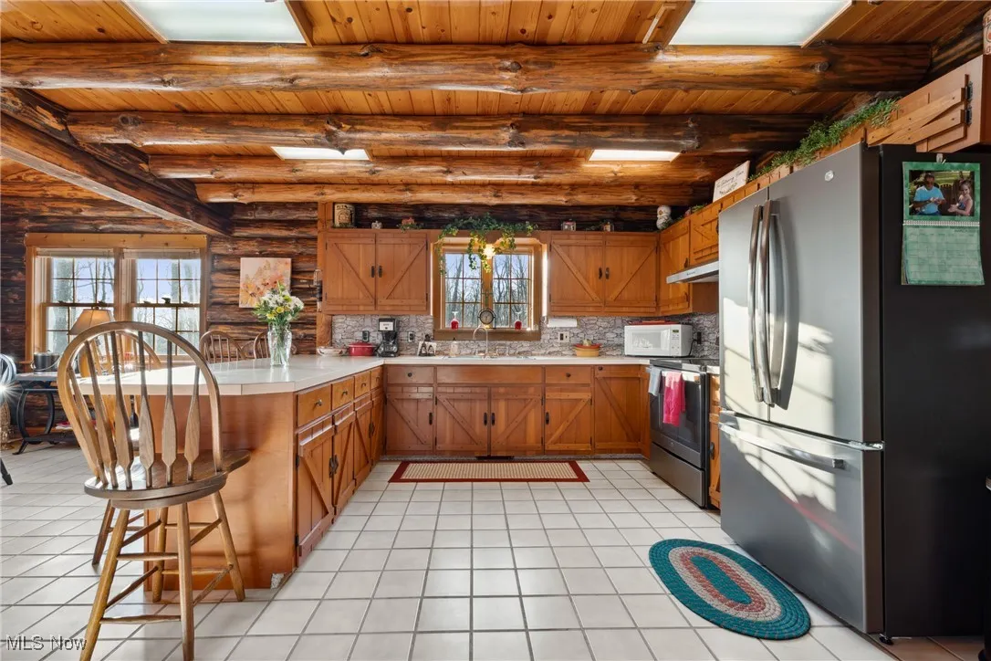 Kitchen with under cabinet range hood, appliances with stainless steel finishes, a peninsula, brown cabinetry, and light countertops