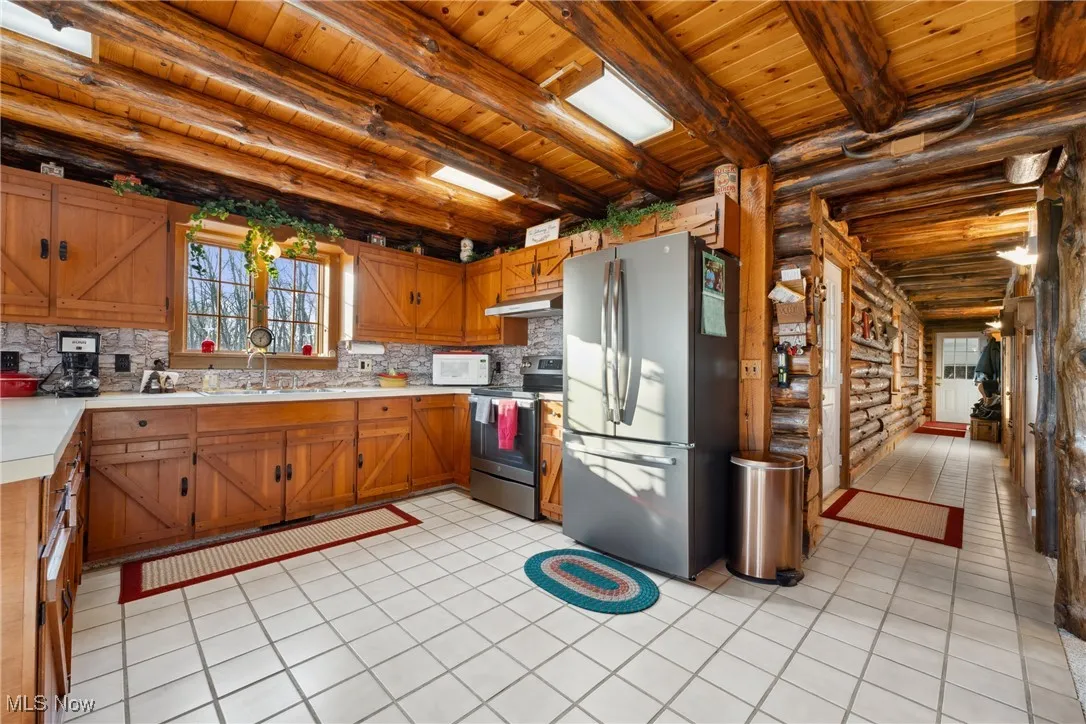 Kitchen with a sink, light countertops, under cabinet range hood, appliances with stainless steel finishes, and wooden ceiling