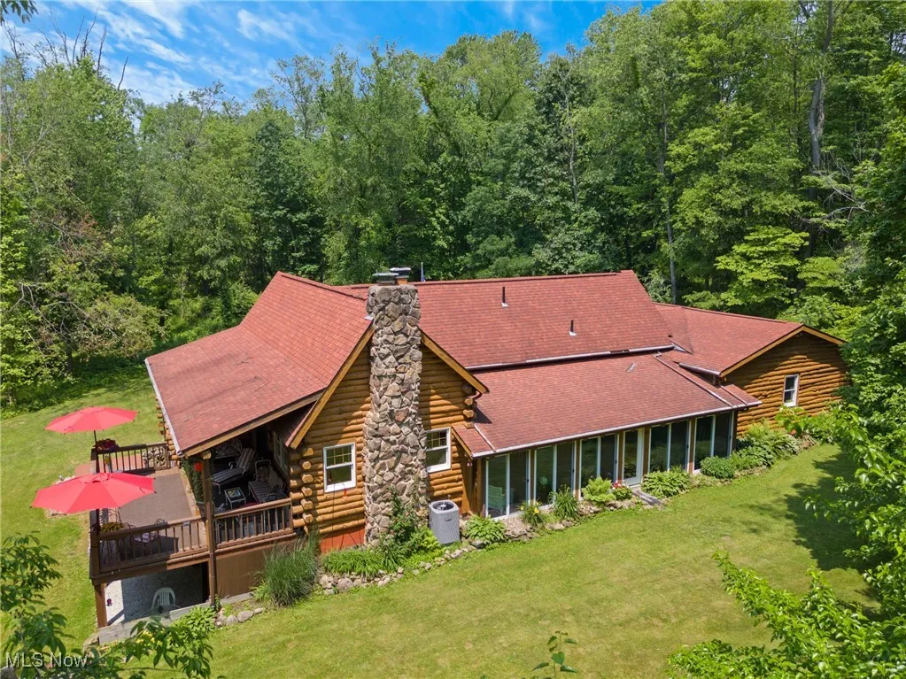 Rear view of property with log siding, a deck, a lawn, and a chimney