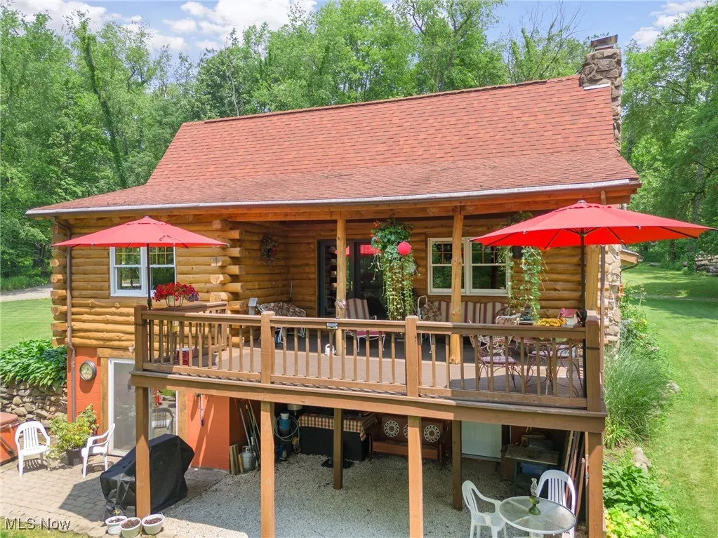 View of front of property featuring log exterior, a deck, a chimney, a carport, and a front lawn