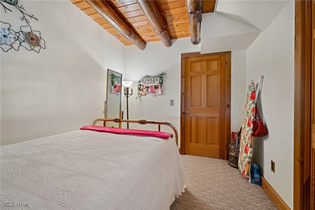 Bedroom with wooden ceiling, lofted ceiling with beams, and carpet floors