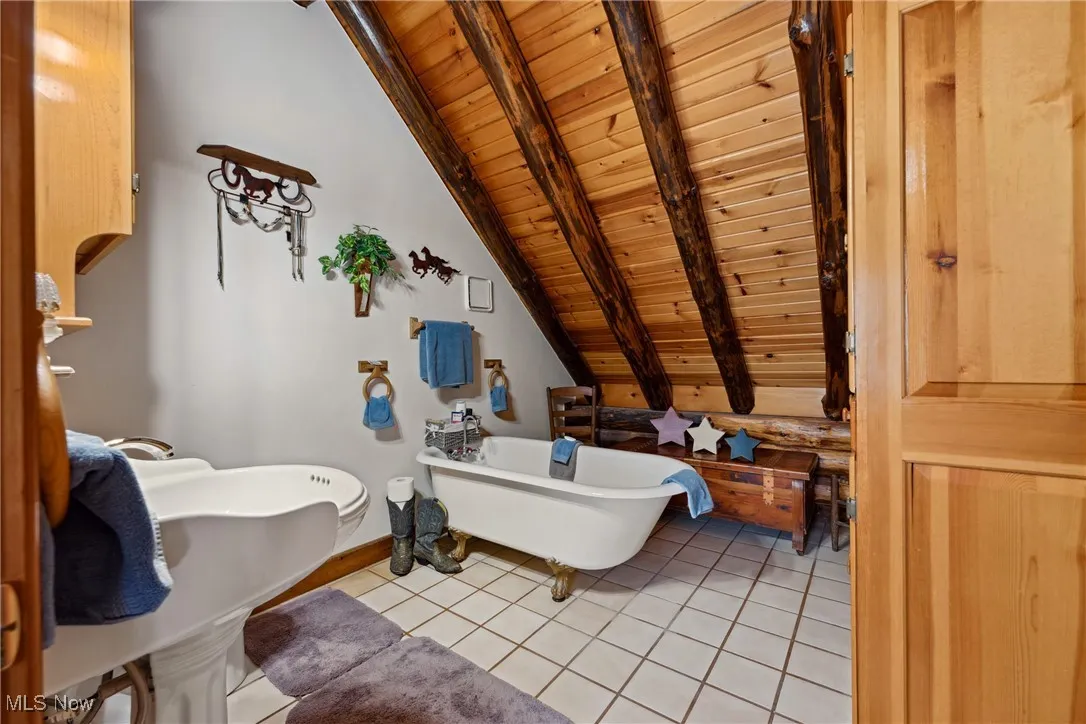 Full bath with baseboards, lofted ceiling with beams, wooden ceiling, tile patterned floors, and a soaking tub
