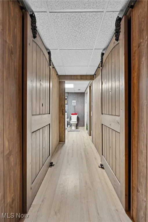 Hallway with wood finished floors, wood walls, and a paneled ceiling
