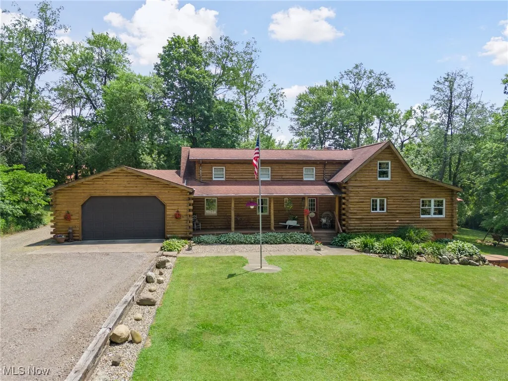Cabin featuring log exterior, covered porch, driveway, and a garage