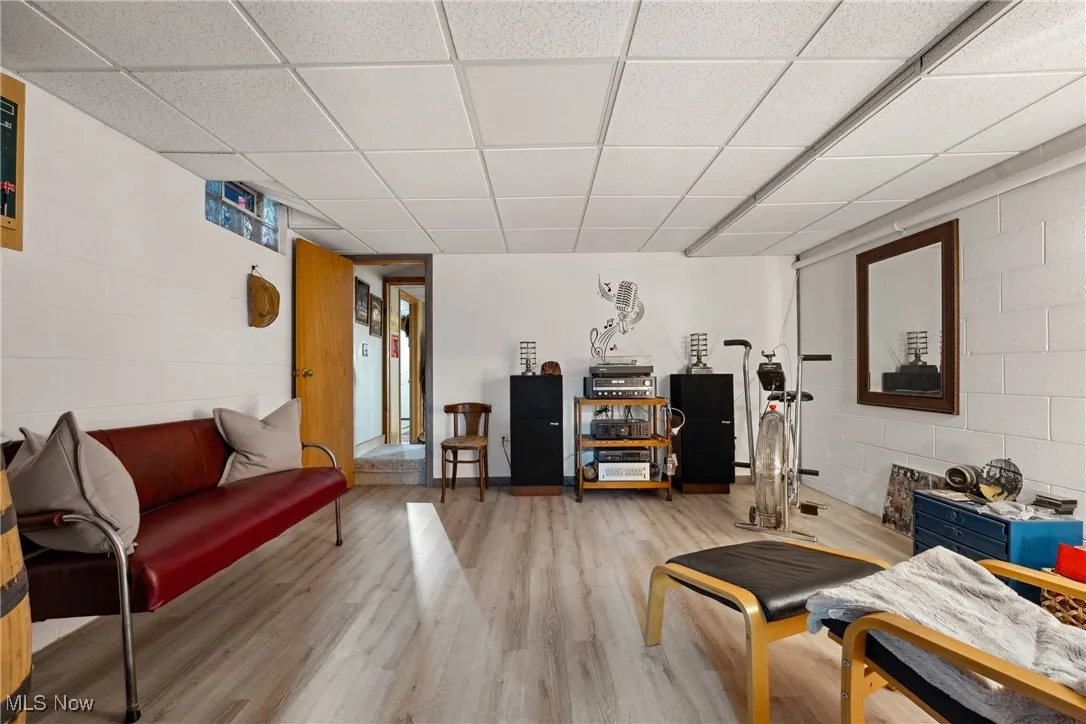 Living room featuring light wood finished floors, a drop ceiling, and concrete block wall