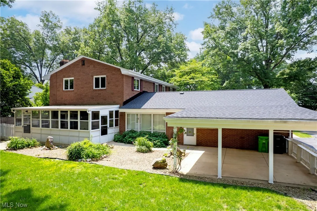 Rear view of property featuring a sunroom, brick siding, a lawn, and a patio area