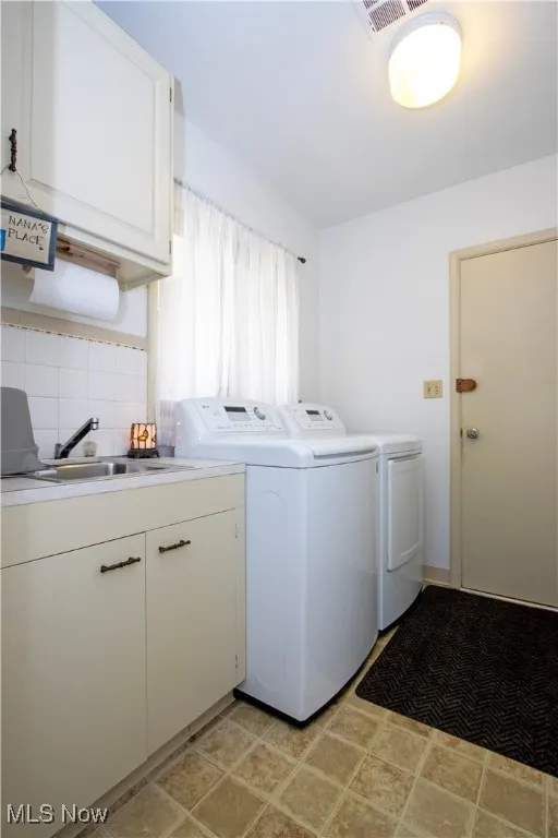 Laundry room with washing machine and dryer, cabinet space, a sink, and visible vents