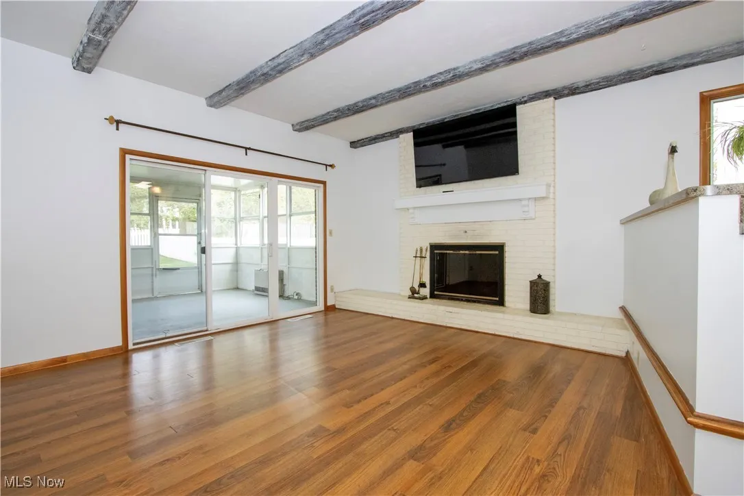 Unfurnished living room featuring a wealth of natural light, a fireplace, wood finished floors, and beam ceiling