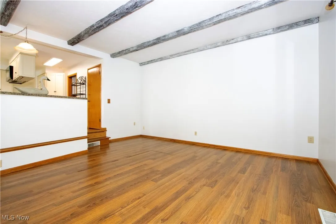 Unfurnished living room featuring baseboards, wood finished floors, visible vents, and beam ceiling