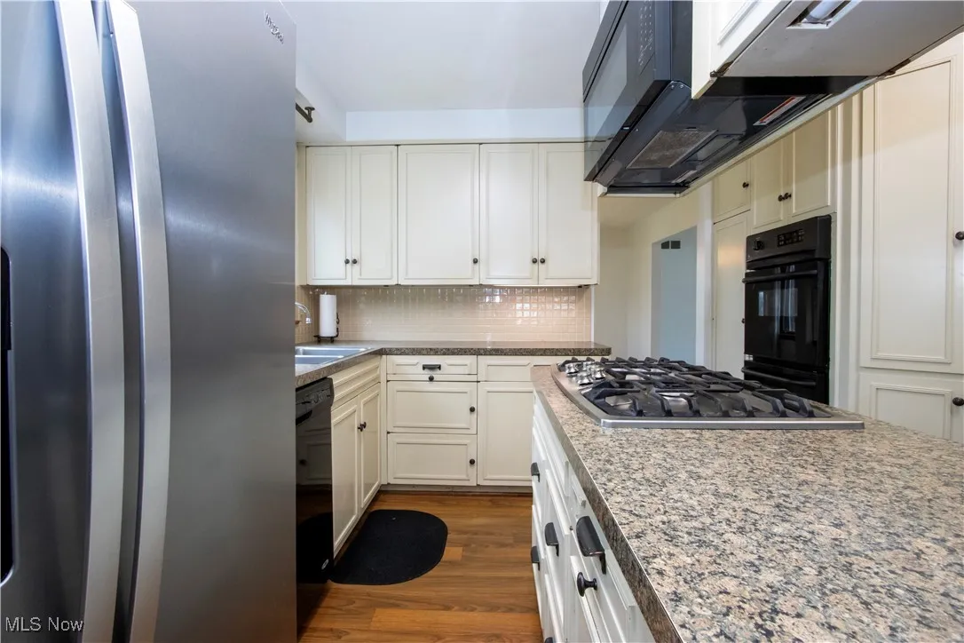 Kitchen with tasteful backsplash, a sink, black appliances, dark wood finished floors, and white cabinetry