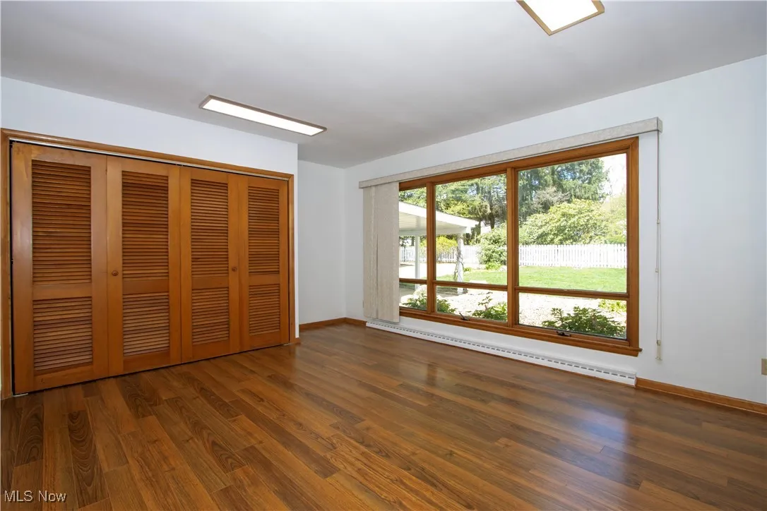 Unfurnished bedroom with a baseboard heating unit, baseboards, wood finished floors, and a closet