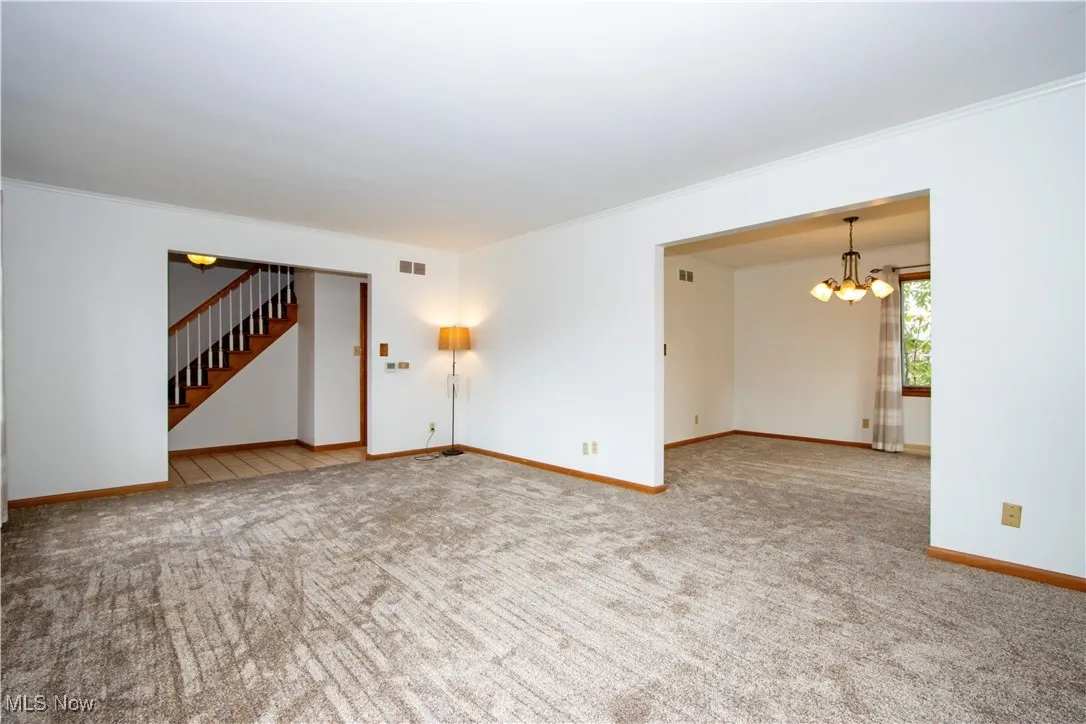 Unfurnished living room with baseboards, carpet, a chandelier, stairway, and crown molding