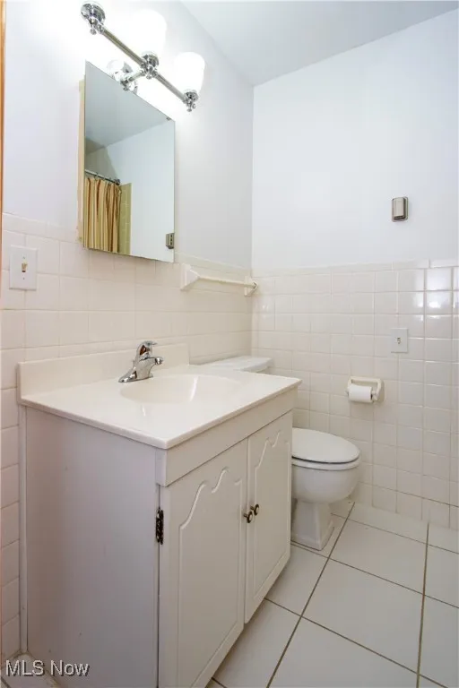 Bathroom featuring tile patterned flooring, toilet, vanity, tile walls, and wainscoting