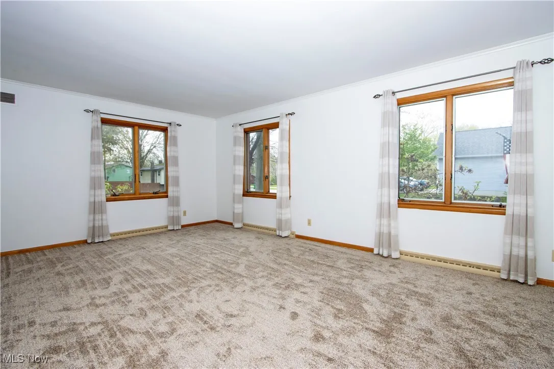 Carpeted empty room featuring a baseboard radiator, visible vents, baseboards, and ornamental molding