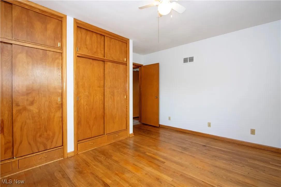 Unfurnished bedroom with a ceiling fan, light wood-style floors, two closets, baseboards, and visible vents