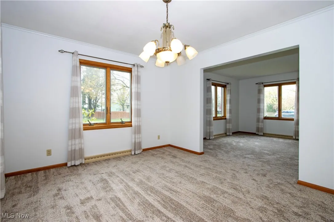 Unfurnished room featuring a chandelier, carpet, a baseboard radiator, and ornamental molding