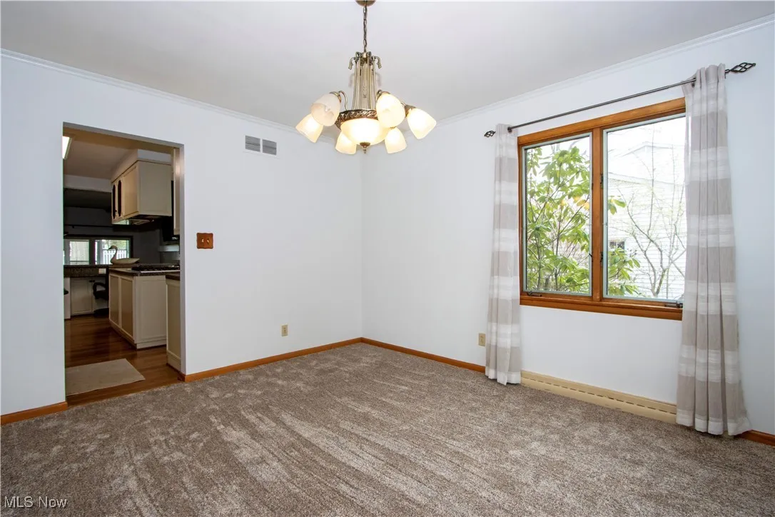 Empty room featuring carpet, visible vents, crown molding, baseboards, and a chandelier