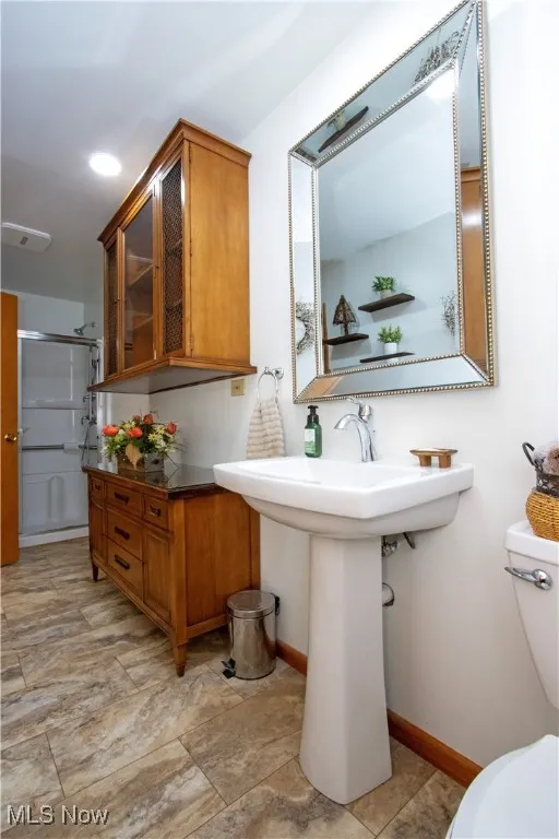 Full bath featuring toilet, baseboards, a stall shower, and a sink