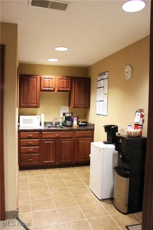 Kitchen featuring dark countertops, visible vents, light tile patterned floors, a sink, and white microwave
