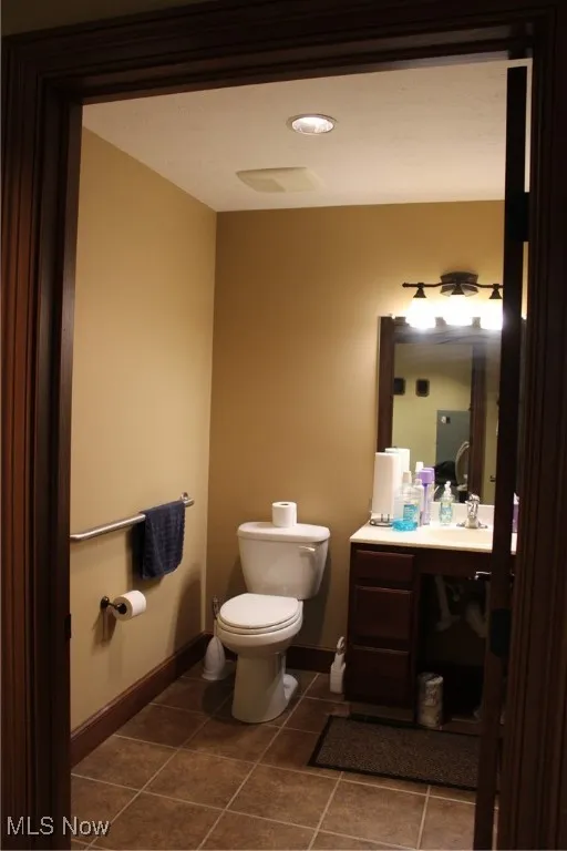 Half bath featuring tile patterned floors, baseboards, vanity, and toilet