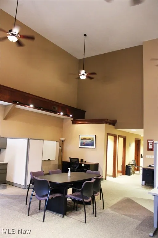 Carpeted dining room with a ceiling fan and a high ceiling