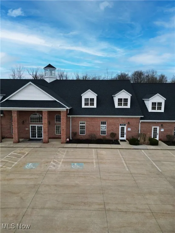 Rear view of property featuring uncovered parking, french doors, brick siding, and roof with shingles