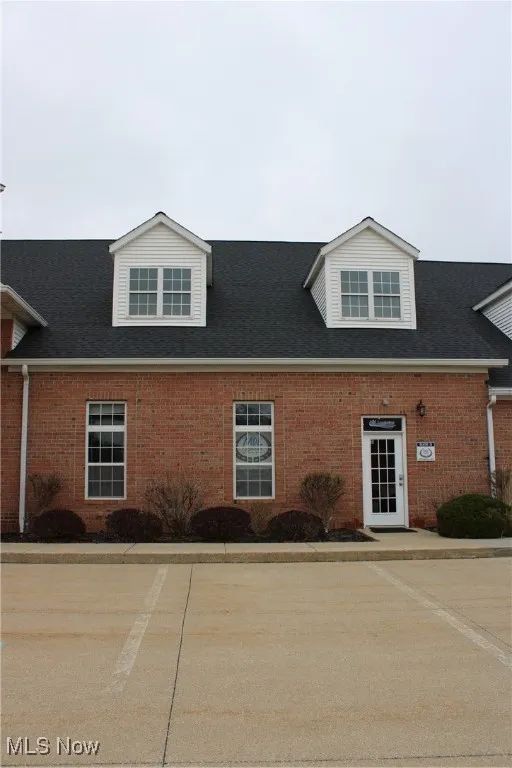 View of front of property featuring brick siding and roof with shingles