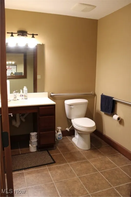Half bath featuring tile patterned flooring, vanity, toilet, and baseboards