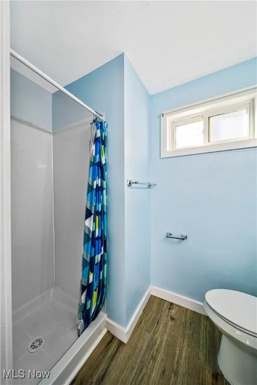 Bathroom with curtained shower, wood-type flooring, and toilet