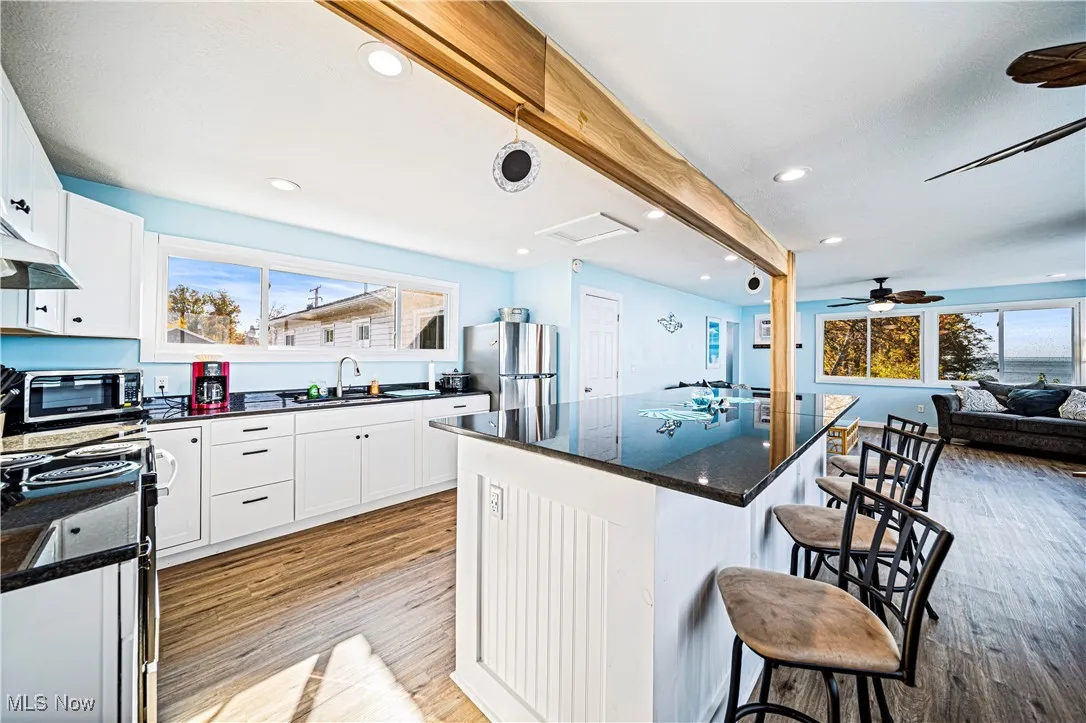 Kitchen with light hardwood / wood-style flooring, a breakfast bar, a kitchen island, ceiling fan, and white cabinets
