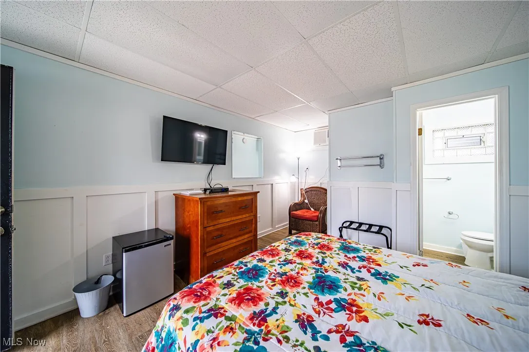 Bedroom featuring hardwood / wood-style floors, fridge, connected bathroom, and a drop ceiling