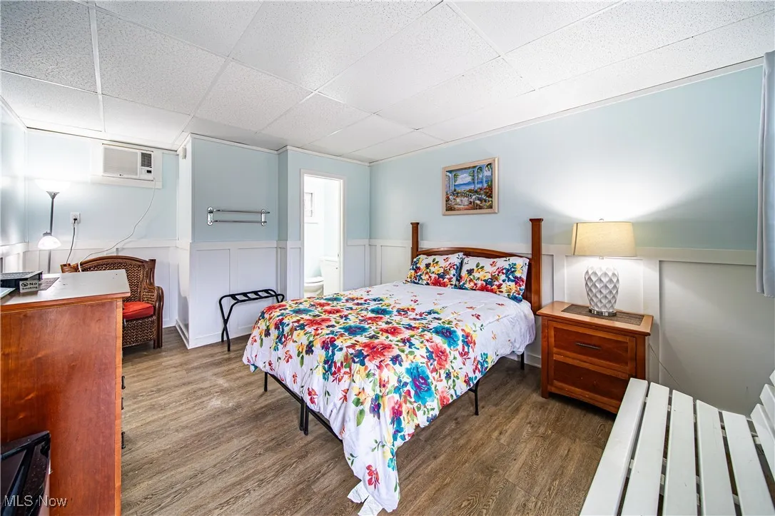 Bedroom featuring dark wood-type flooring, a drop ceiling, and an AC wall unit