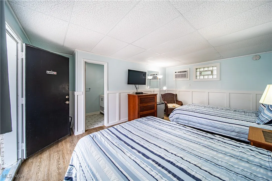 Bedroom with a paneled ceiling, light hardwood / wood-style floors, connected bathroom, and a wall unit AC