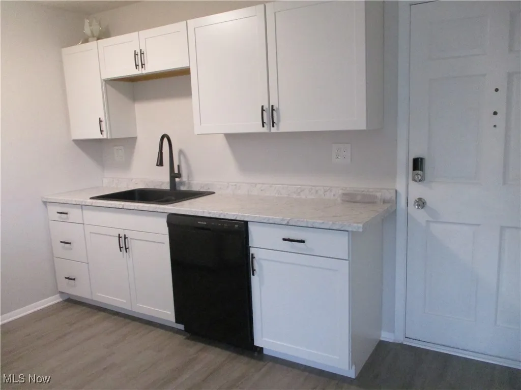 Kitchen featuring black dishwasher, light grey laminate  wood-style floors, light countertops, and a sink with disposal.