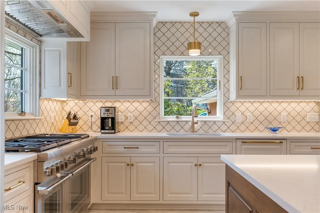 Kitchen featuring light countertops, a sink, range with two ovens, custom exhaust hood, and white cabinetry
