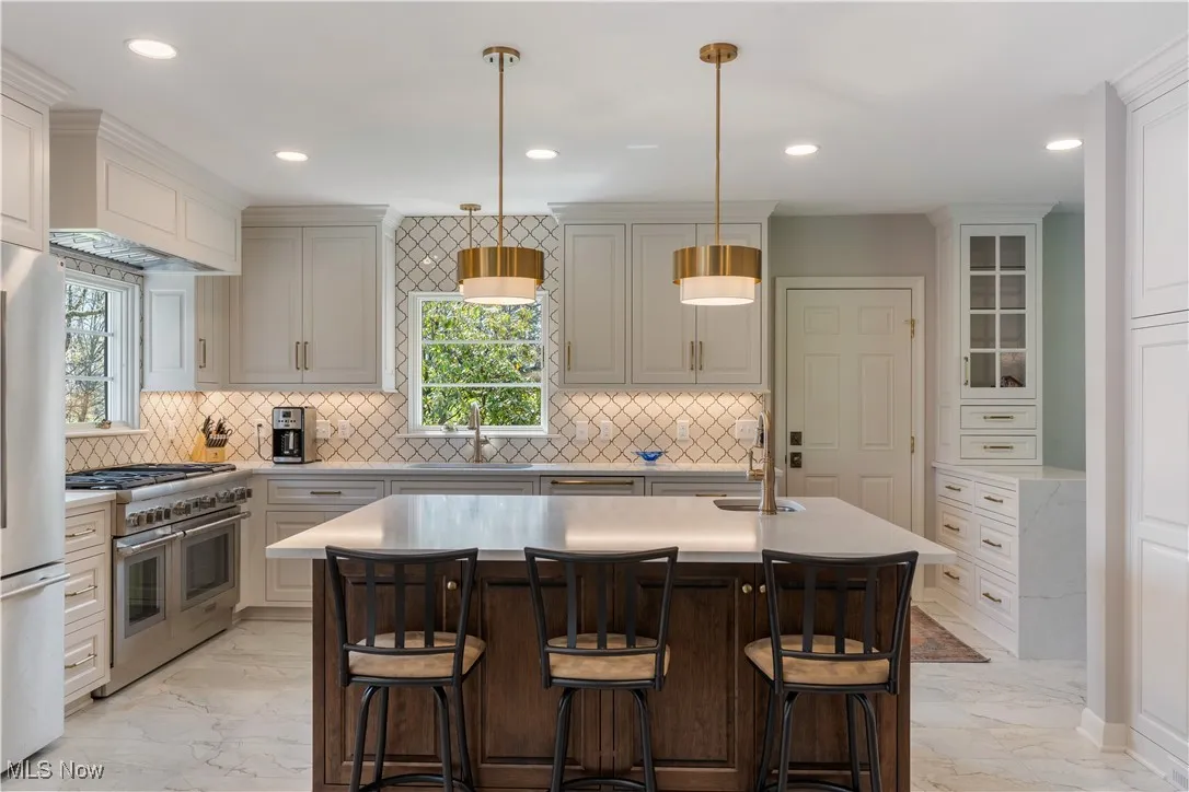 Kitchen with a sink, a kitchen island with sink, marble finish floor, light countertops, and appliances with stainless steel finishes