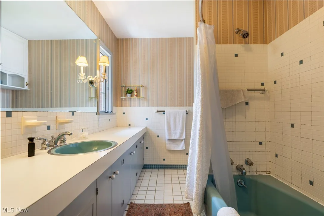 Bathroom featuring tile walls, wallpapered walls, tile patterned flooring, shower / bathtub combination with curtain, and vanity