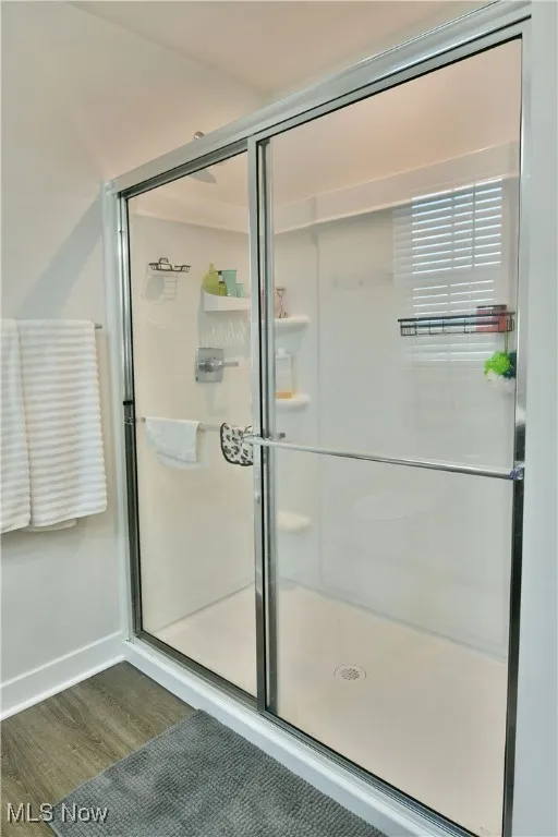 Bathroom featuring baseboards, wood finished floors, and a stall shower
