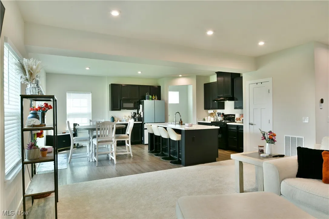Kitchen featuring a sink, black appliances, light wood-type flooring, light countertops, and a kitchen bar