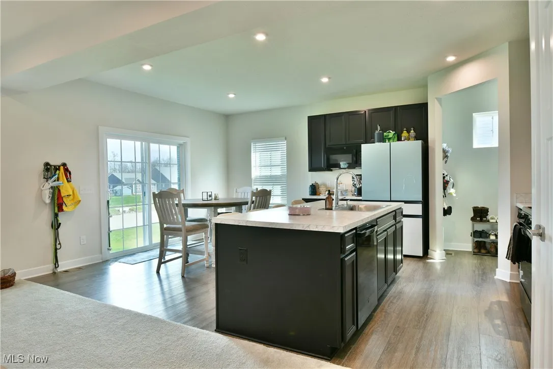 Kitchen featuring wood finished floors, a sink, black microwave, a kitchen island with sink, and light countertops