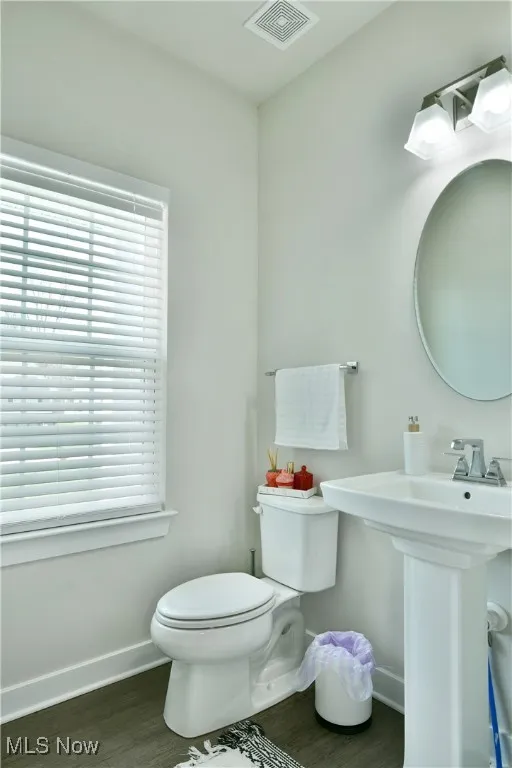 Half bath with plenty of natural light, wood finished floors, visible vents, toilet, and baseboards