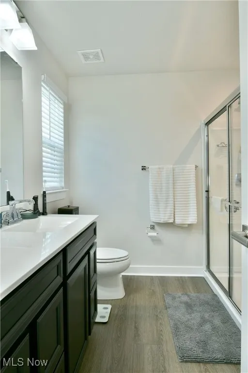 Bathroom with a shower stall, wood finished floors, visible vents, toilet, and vanity