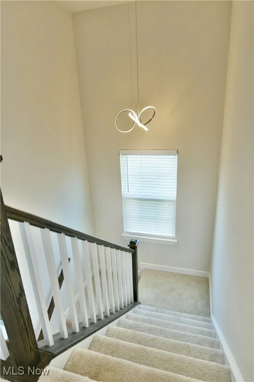 Staircase with baseboards, an inviting chandelier, and carpet flooring