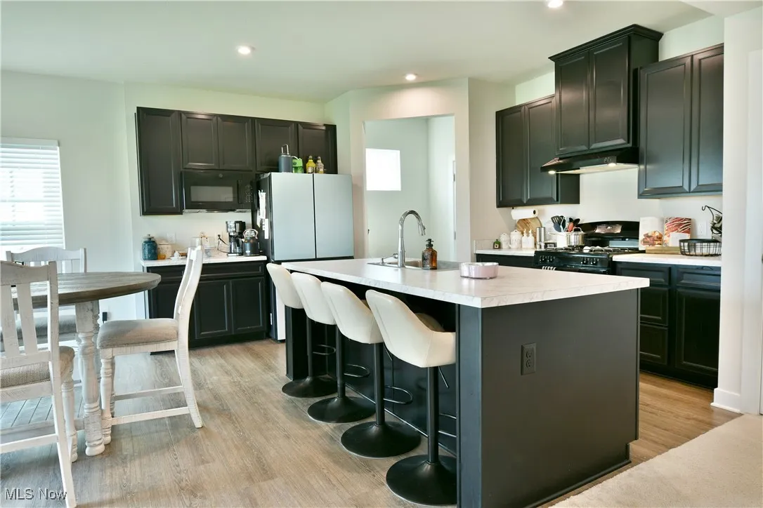 Kitchen with black appliances, light countertops, a center island with sink, light wood-style flooring, and under cabinet range hood