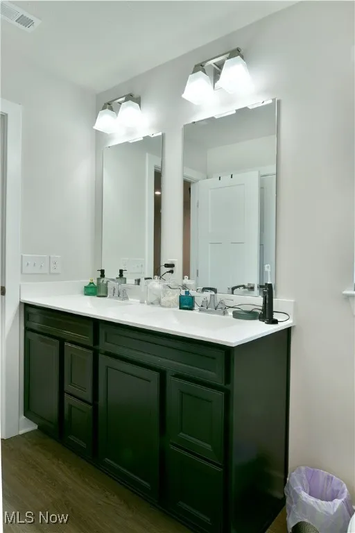 Bathroom with double vanity, wood finished floors, visible vents, and a sink