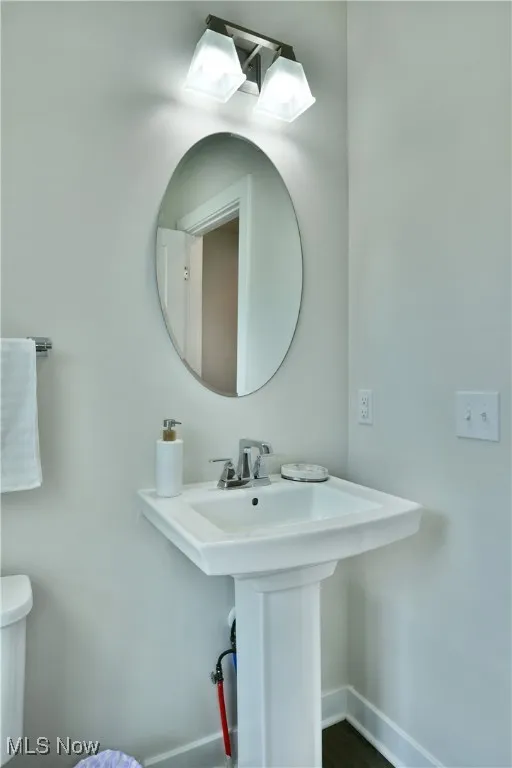 Half bath featuring baseboards, toilet, and a sink