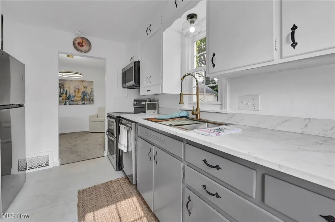 Kitchen featuring appliances with stainless steel finishes, gray cabinetry, a sink, baseboards, and light stone countertops