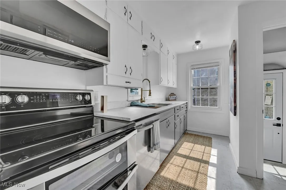 Kitchen with appliances with stainless steel finishes, a sink, white cabinetry, light countertops, and baseboards