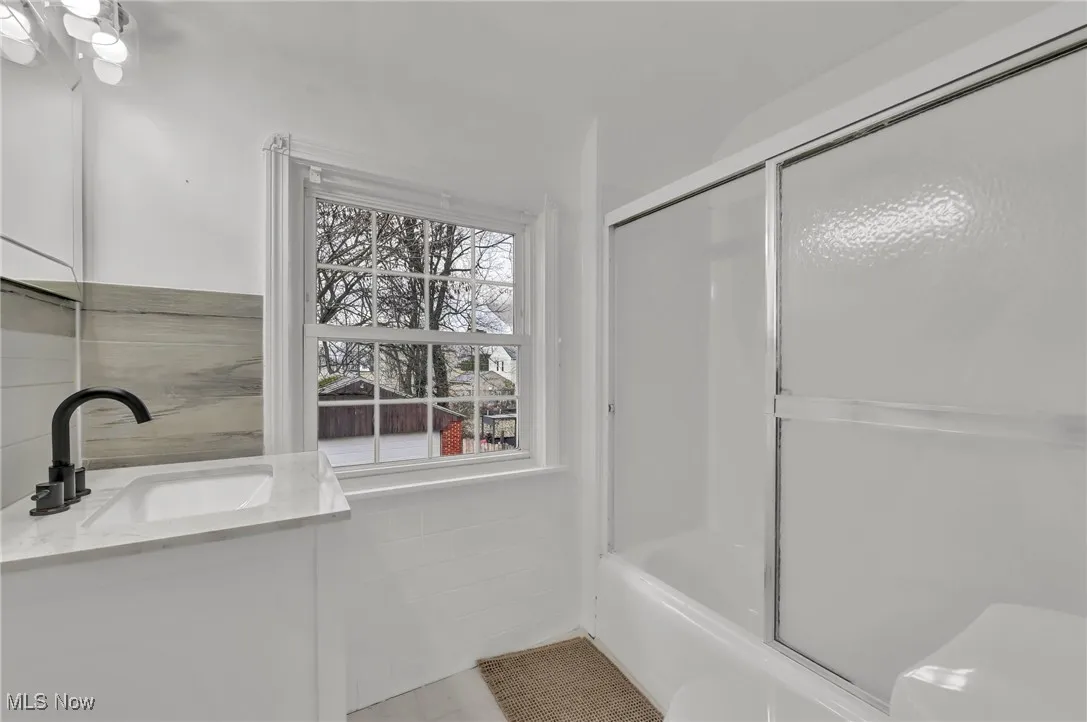 Bathroom featuring shower / bath combination with glass door, tile patterned floors, vanity, and toilet